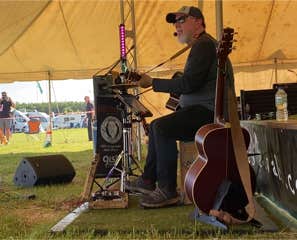 Ginger Geoffrey at Wild Festival Litchfield sat on a cajonwearing a bseball cap and sun glasses.