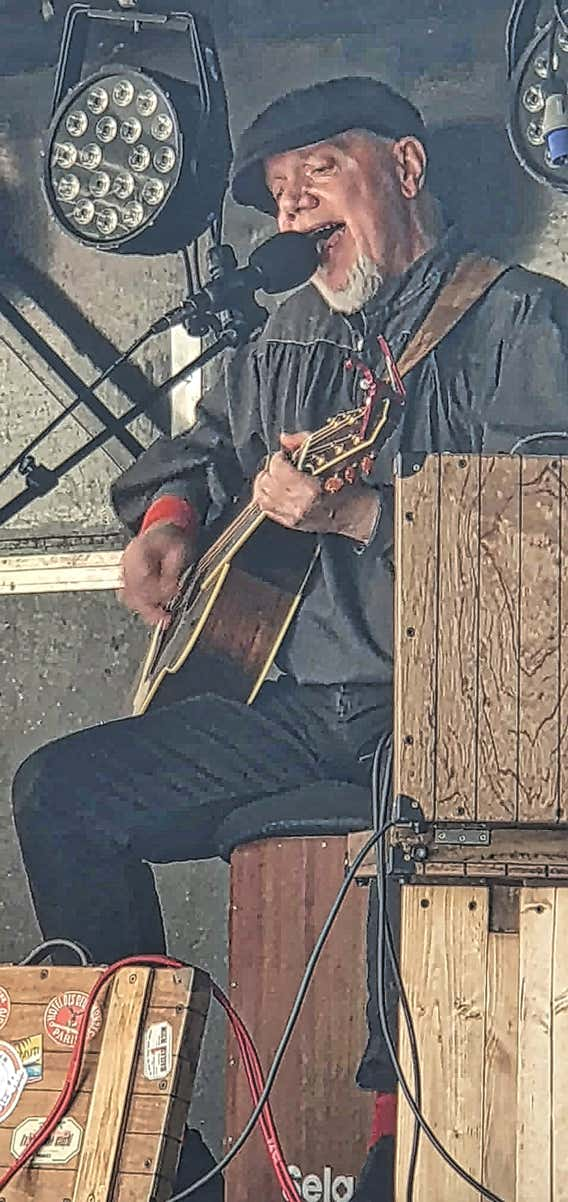 Ginger Geoffrey strumming a guitar and singing into a microphone