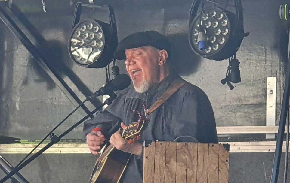 Ginger Geoffrey singing into a microphone while playing guitar